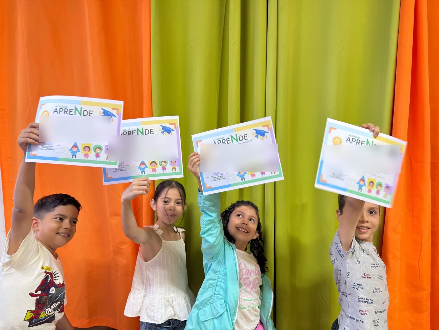 Cuatro niños levantando en alto sus certificados de graduación del curso de inglés de Academia Aprende.