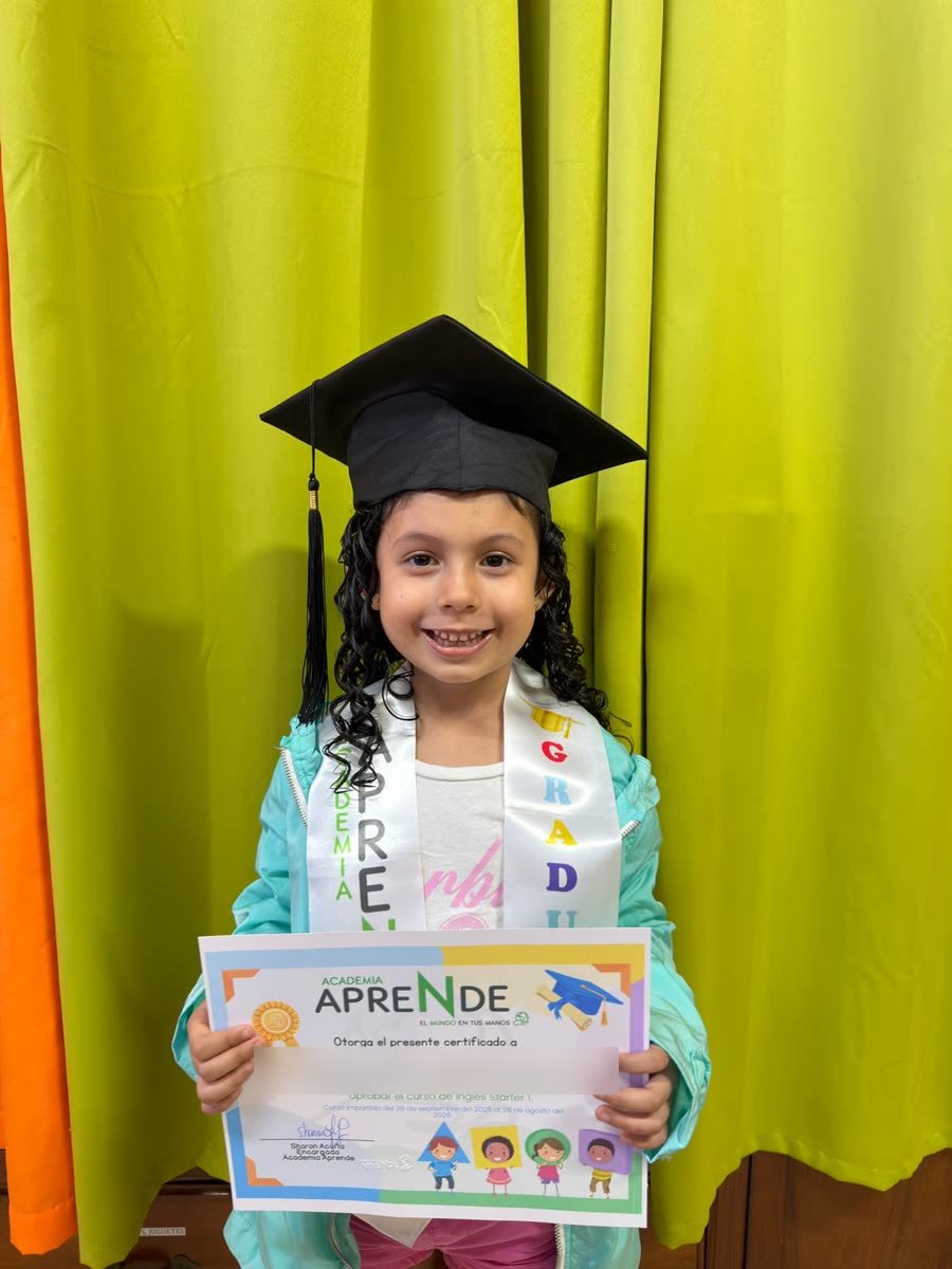 Niña con birrete y banda de graduación sosteniendo su certificado del curso de Inglés Starter 1 de Academia Aprende.